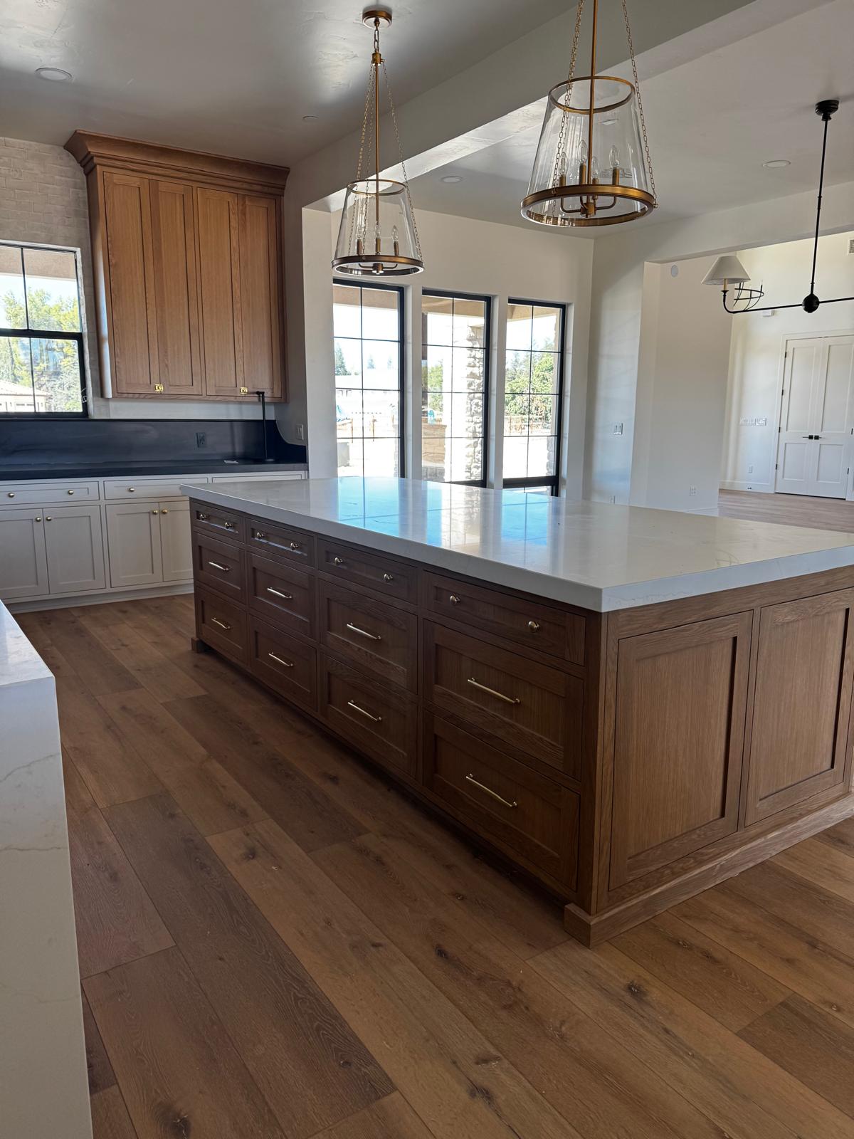 Large stained white oak kitchen island with brass hardware, a quartz countertop and glass pendant lights above