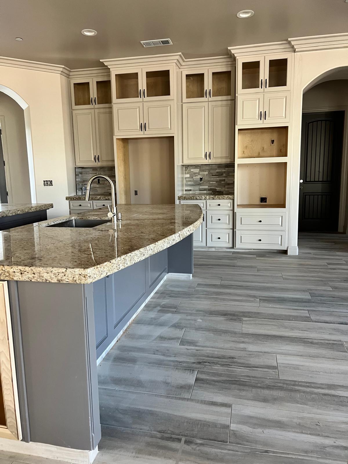 Glazed cream raised-panel kitchen with glass-front stacked uppers, a curved granite bar on a gray painted island and a built-in hutch with open shelving beside an arched doorway
