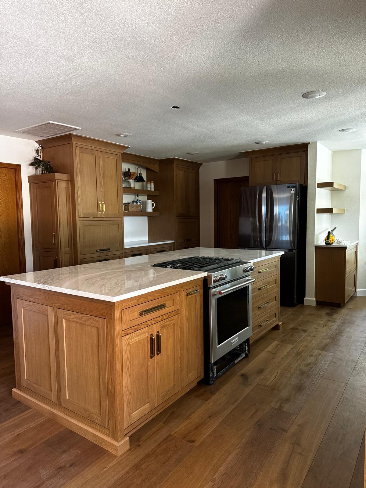 White oak kitchen island with a slide-in range and deep drawer bank, facing a tall oak cabinet wall with an arched niche of open shelves
