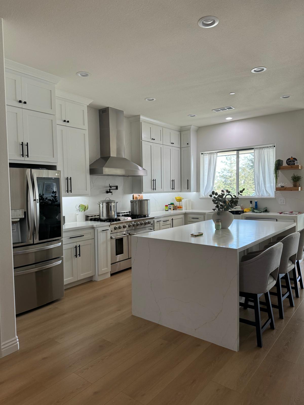 All-white shaker kitchen with stacked uppers, a stainless hood and pot filler, and a large quartz waterfall island seating four