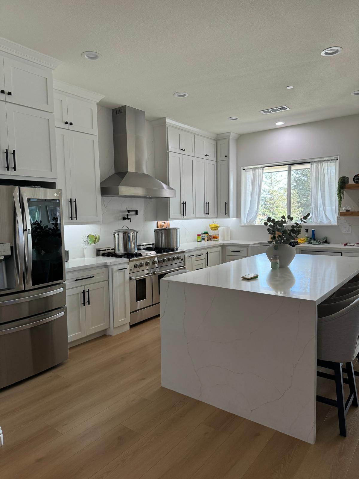 Bright all-white shaker kitchen with stacked uppers, a stainless hood and a quartz waterfall island