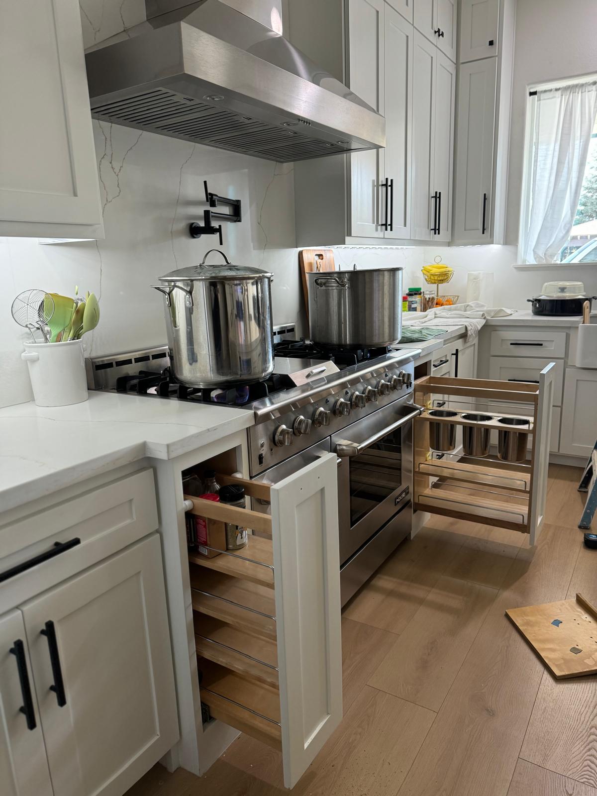 Two narrow maple pull-out storage racks extended on either side of a professional range in a white kitchen